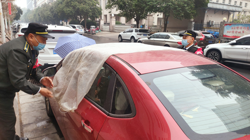 郑州街头一辆轿车天窗大开，巡防队员用塑料布将其盖住防雨淋